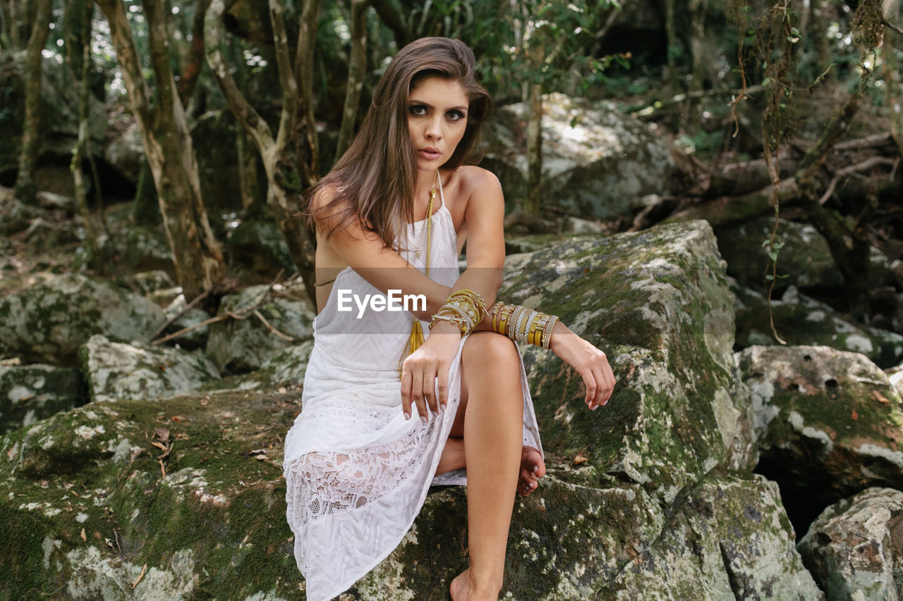 Portrait of young woman sitting on rock in forest