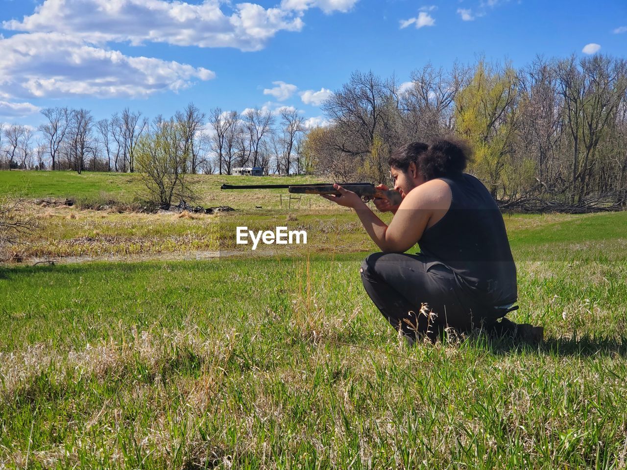 Side view of man kneeling in the country field with a rifle