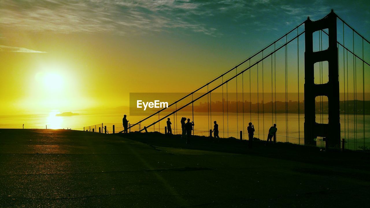 Silhouettes of people by suspension bridge