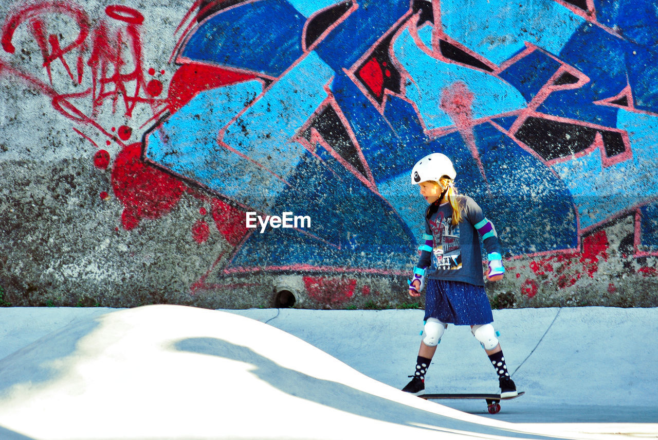 Girl skating against old graffiti wall