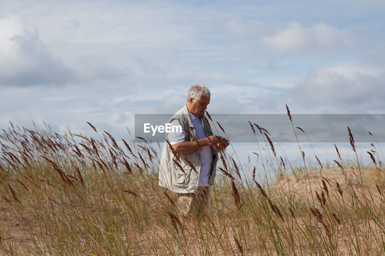 Mature man standing on field against sky