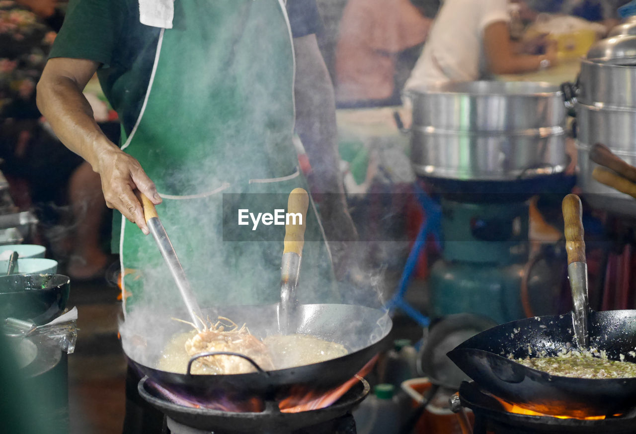 REFLECTION OF PEOPLE IN COOKING PAN ON BARBECUE GRILL