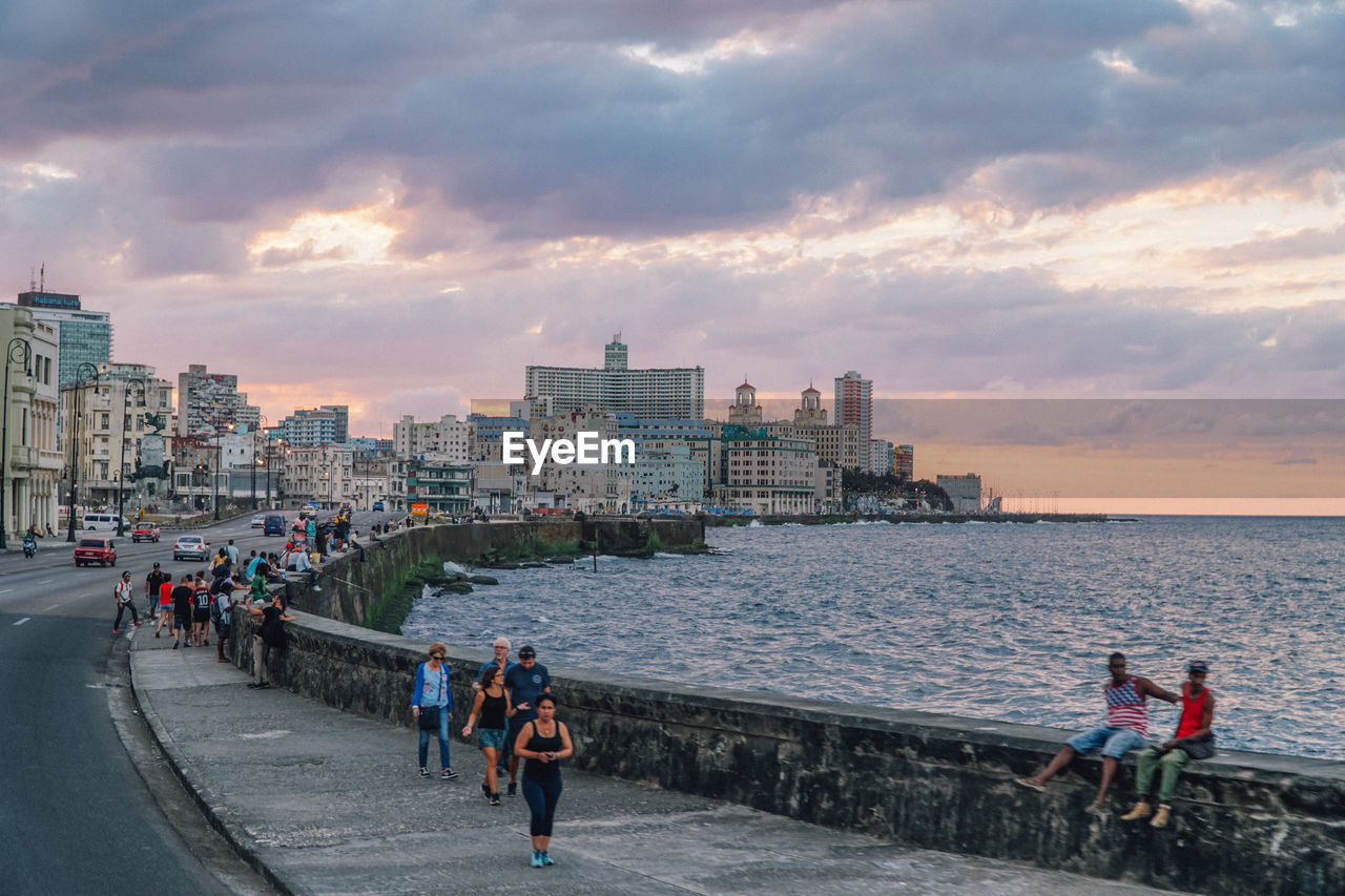 PEOPLE BY SEA AGAINST SKY DURING SUNSET