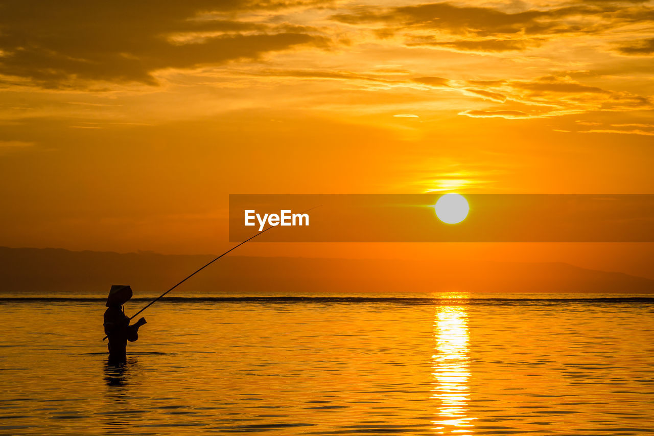 Silhouette man fishing in sea against sky during sunset