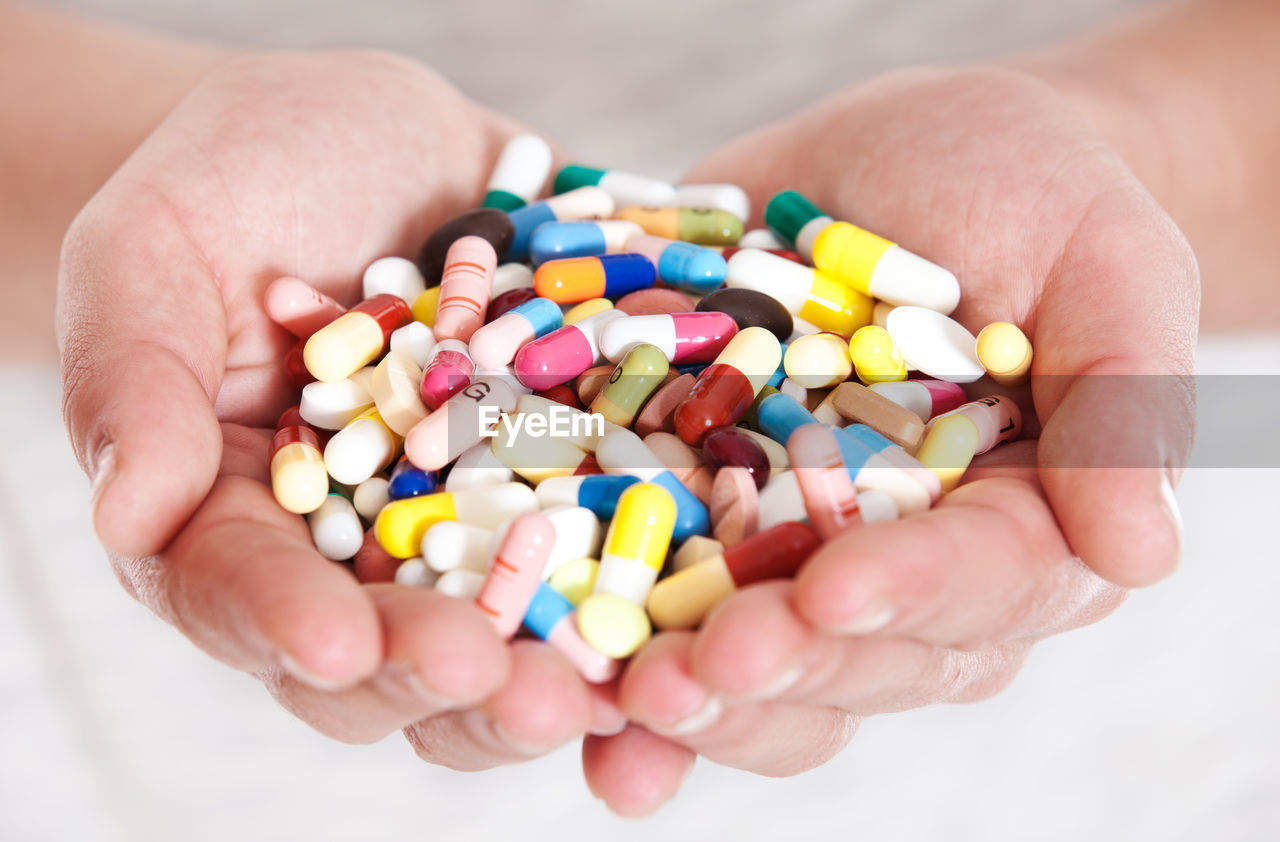 Cropped image of hands holding pills an capsules against white background