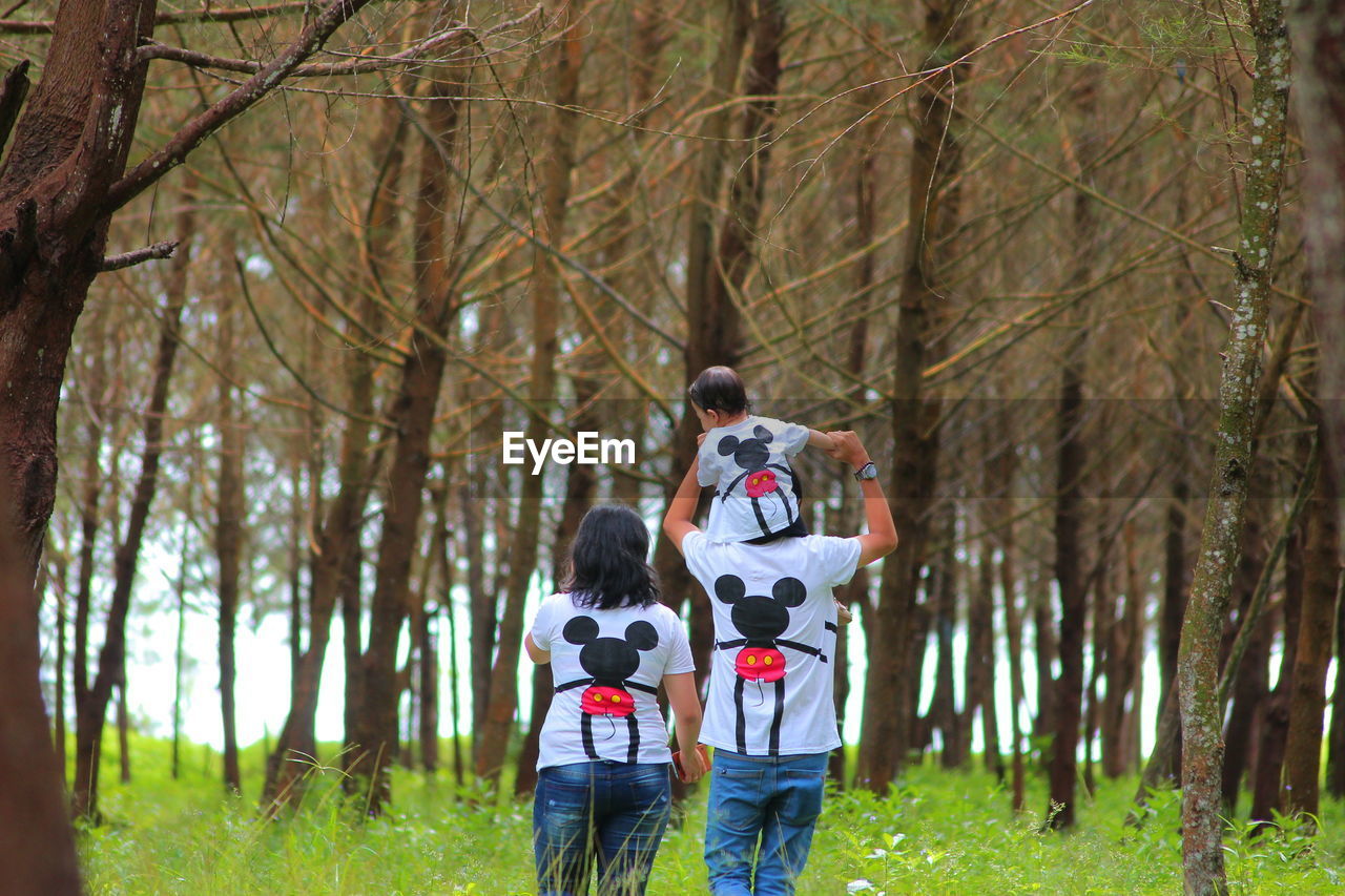 REAR VIEW OF TWO PEOPLE STANDING IN FOREST