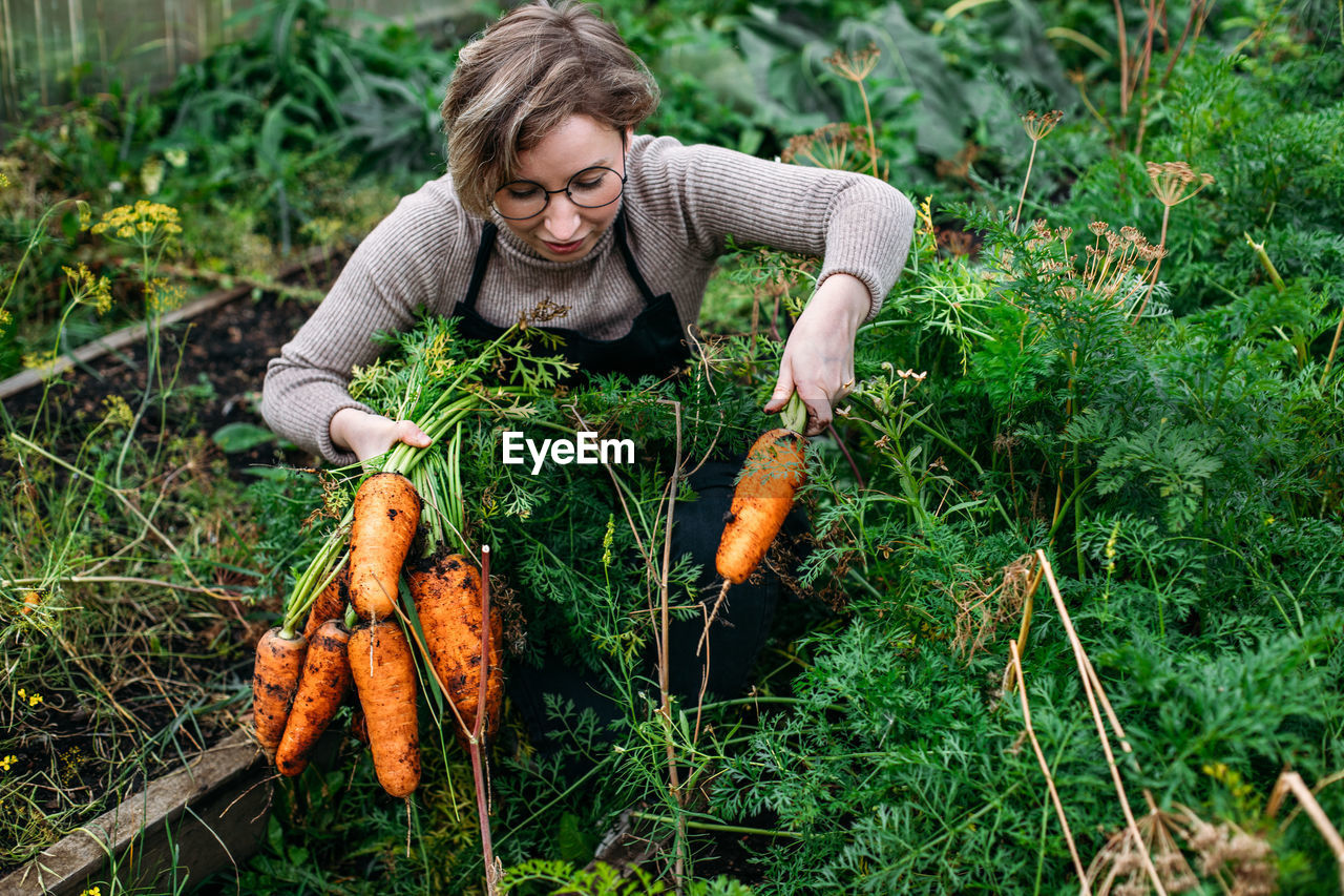 Smiling woman holding carrots at farm