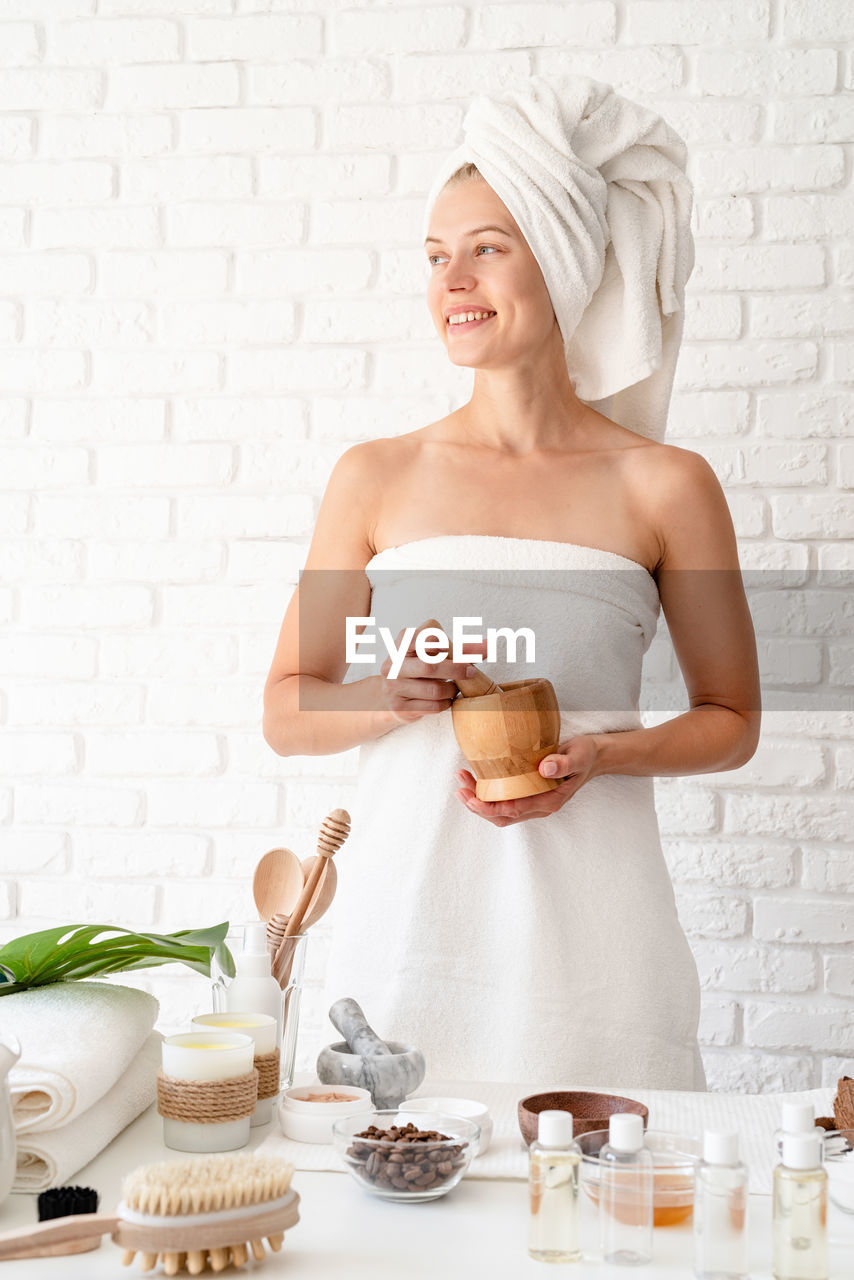 Woman wearing white bathrobes towels on head doing spa procedures mixing natural ingredients