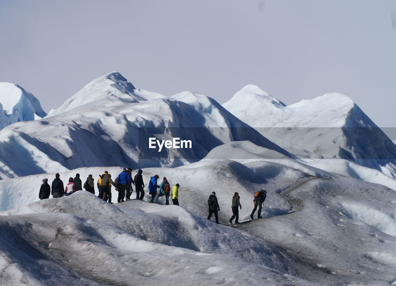 Hikers on snowcapped mountain against sky