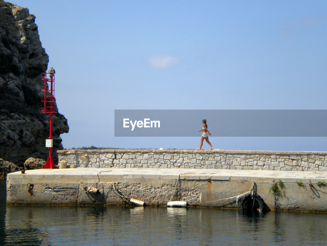 Full length of woman walking on retaining wall by lake against sky