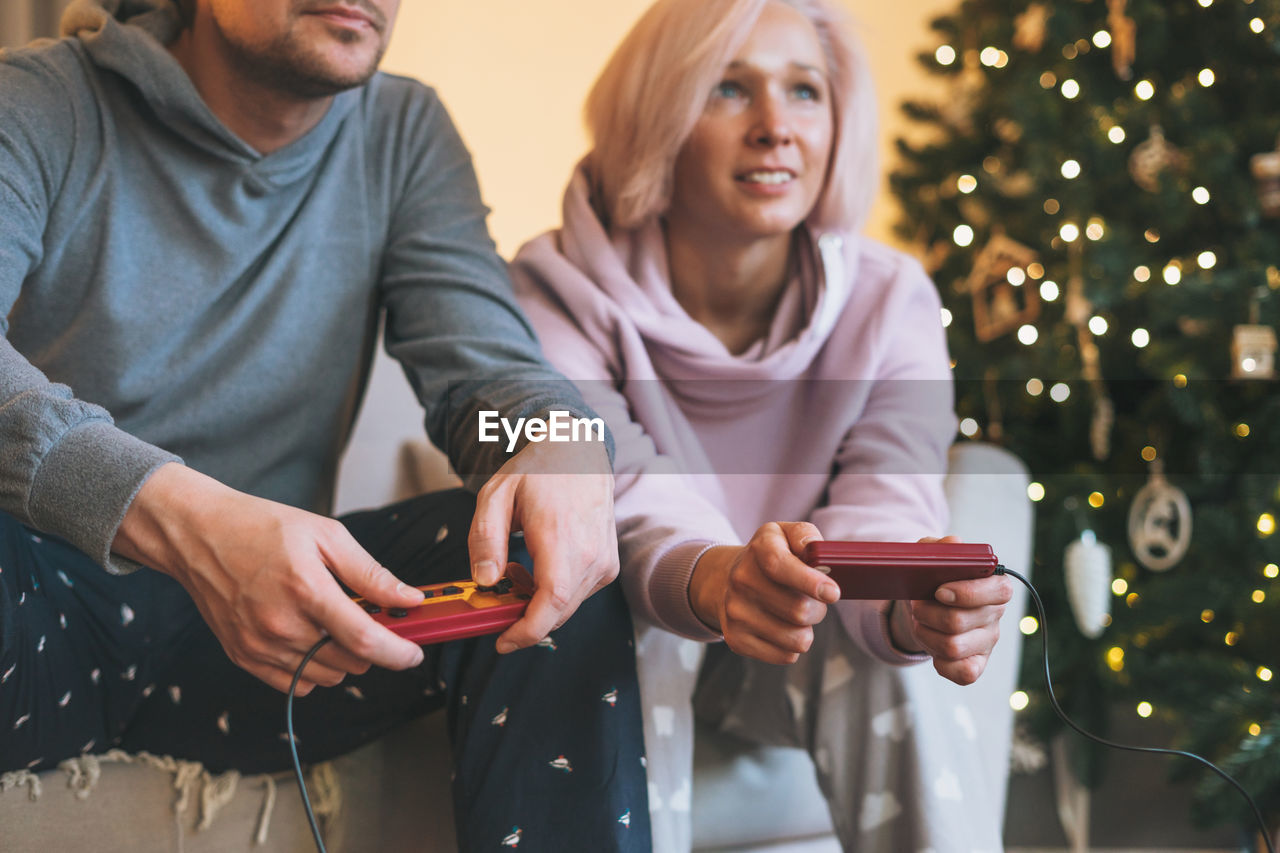 Crop photo of young family in home clothes playing video games on couch on background 