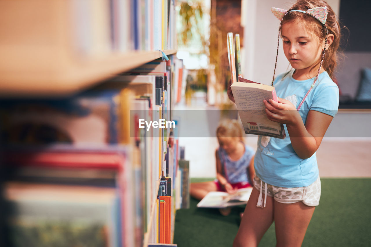 Schoolgirls looking for book for reading in school library. students choosing books for reading