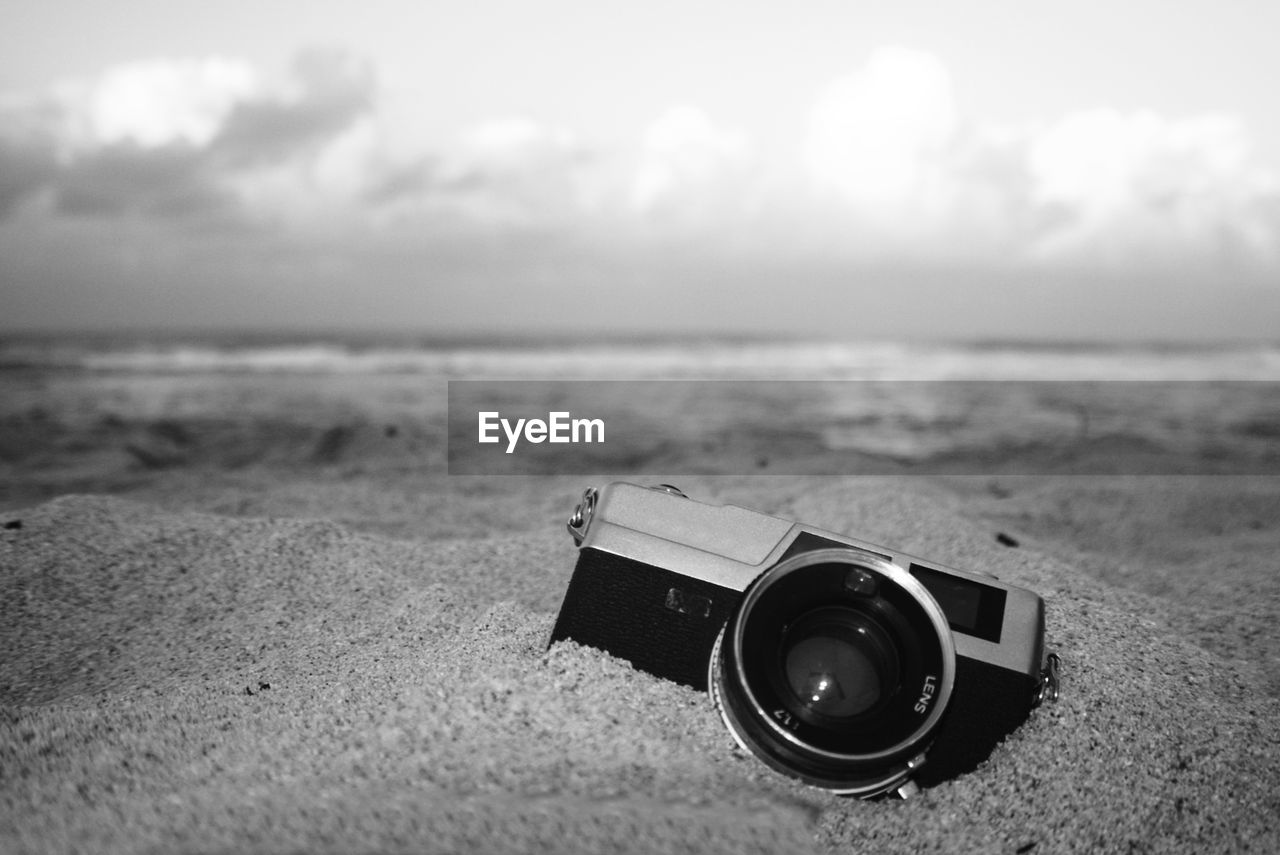 Close-up of camera on sand at beach against sky