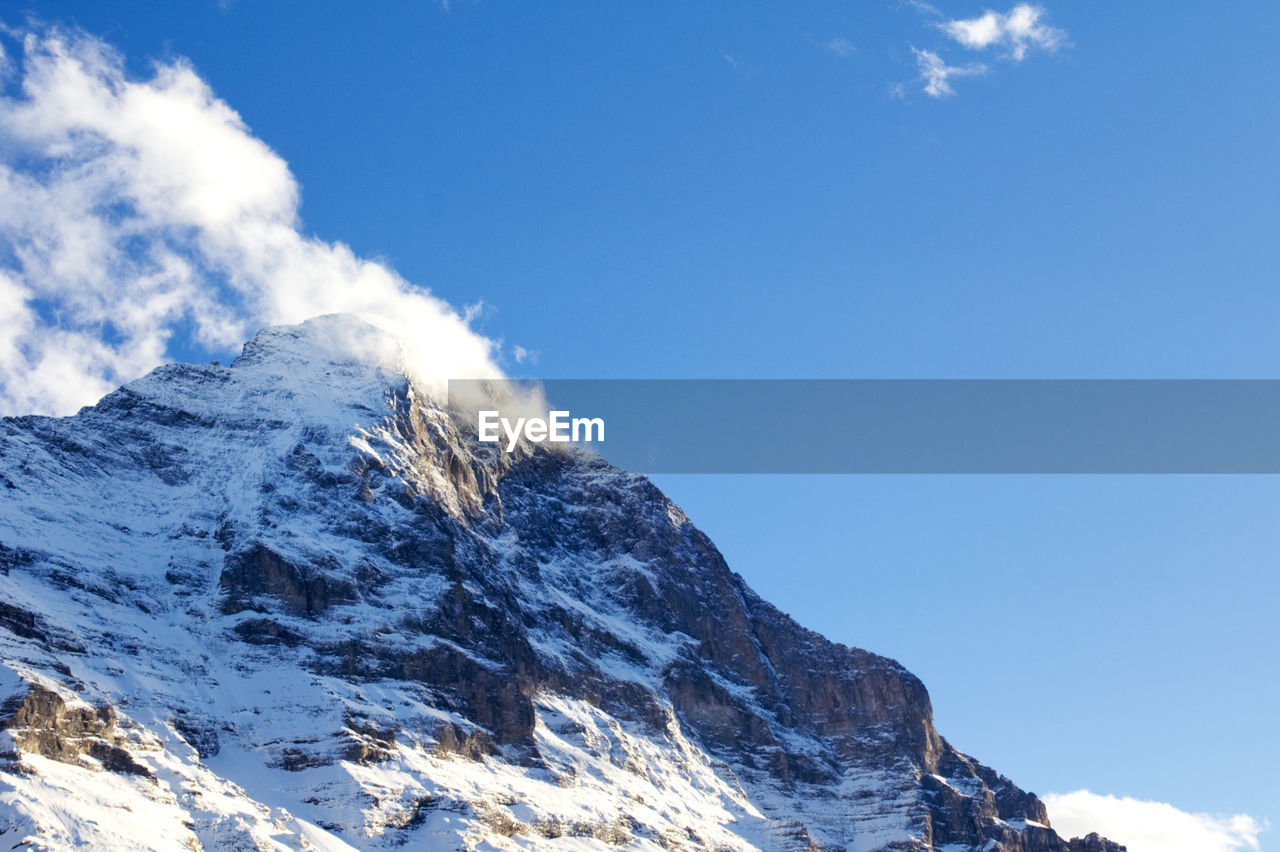 Low angle view of snowcapped mountains against blue sky