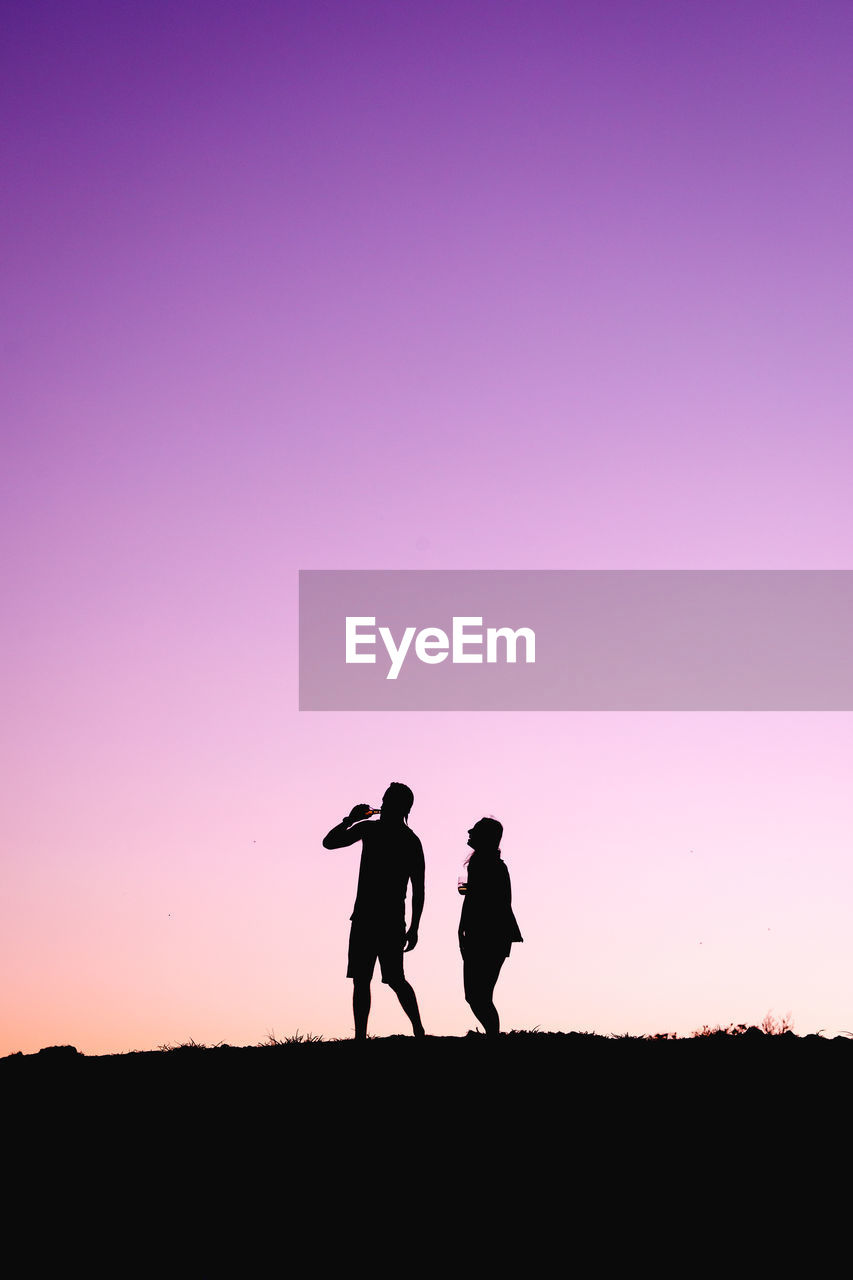 Silhouette friends standing on field against sky during sunset