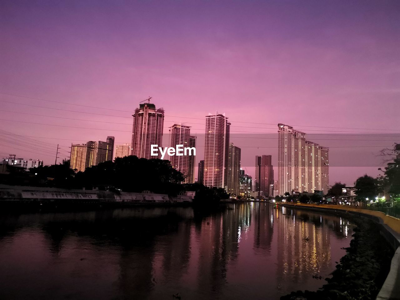 River by illuminated buildings against sky at sunset