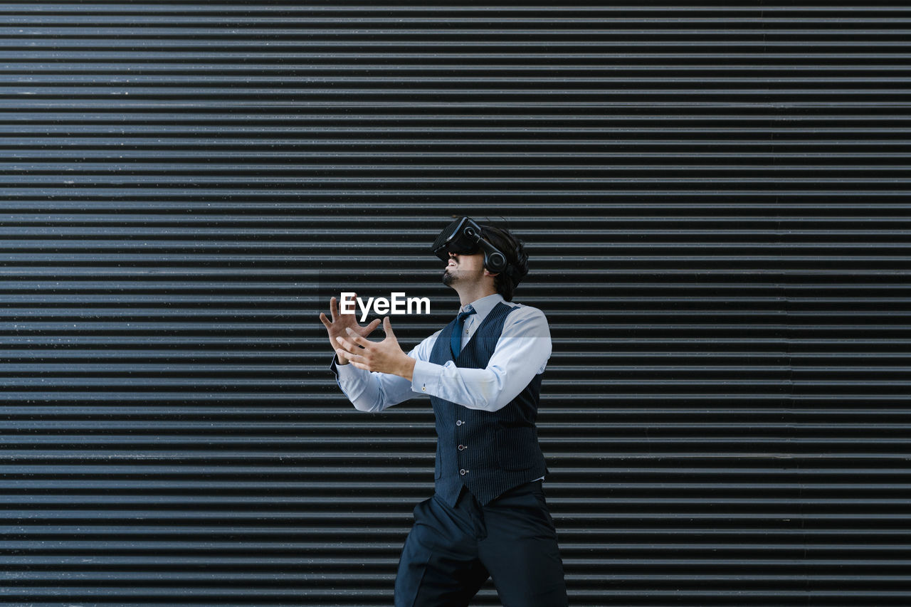 Businessman gesturing while watching movie through virtual reality simulator against black wall