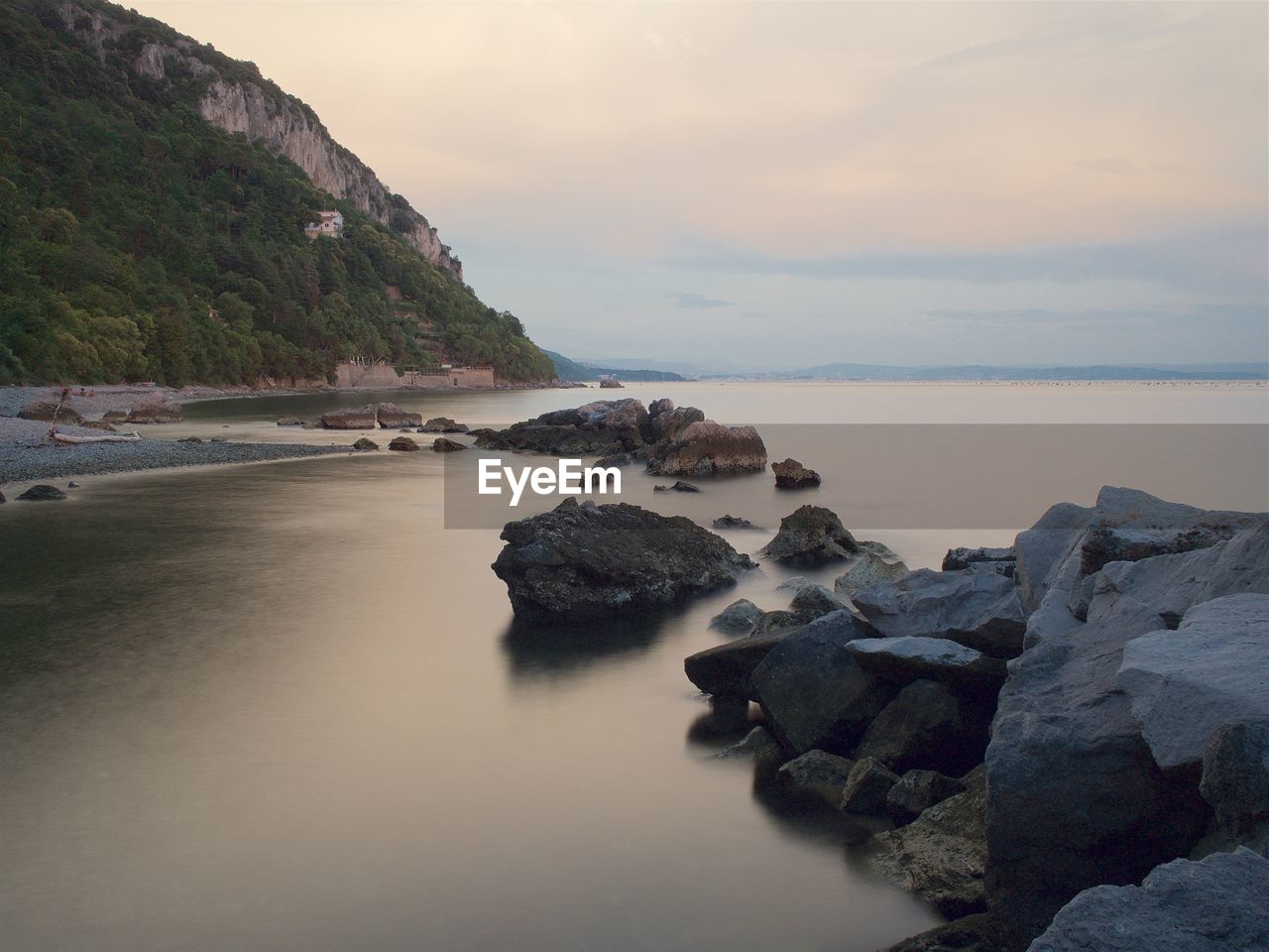 Scenic view of stones next to sea against cloudy sky