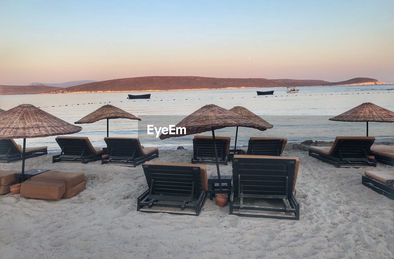 Empty chairs and parasols at beach against clear sky during sunset