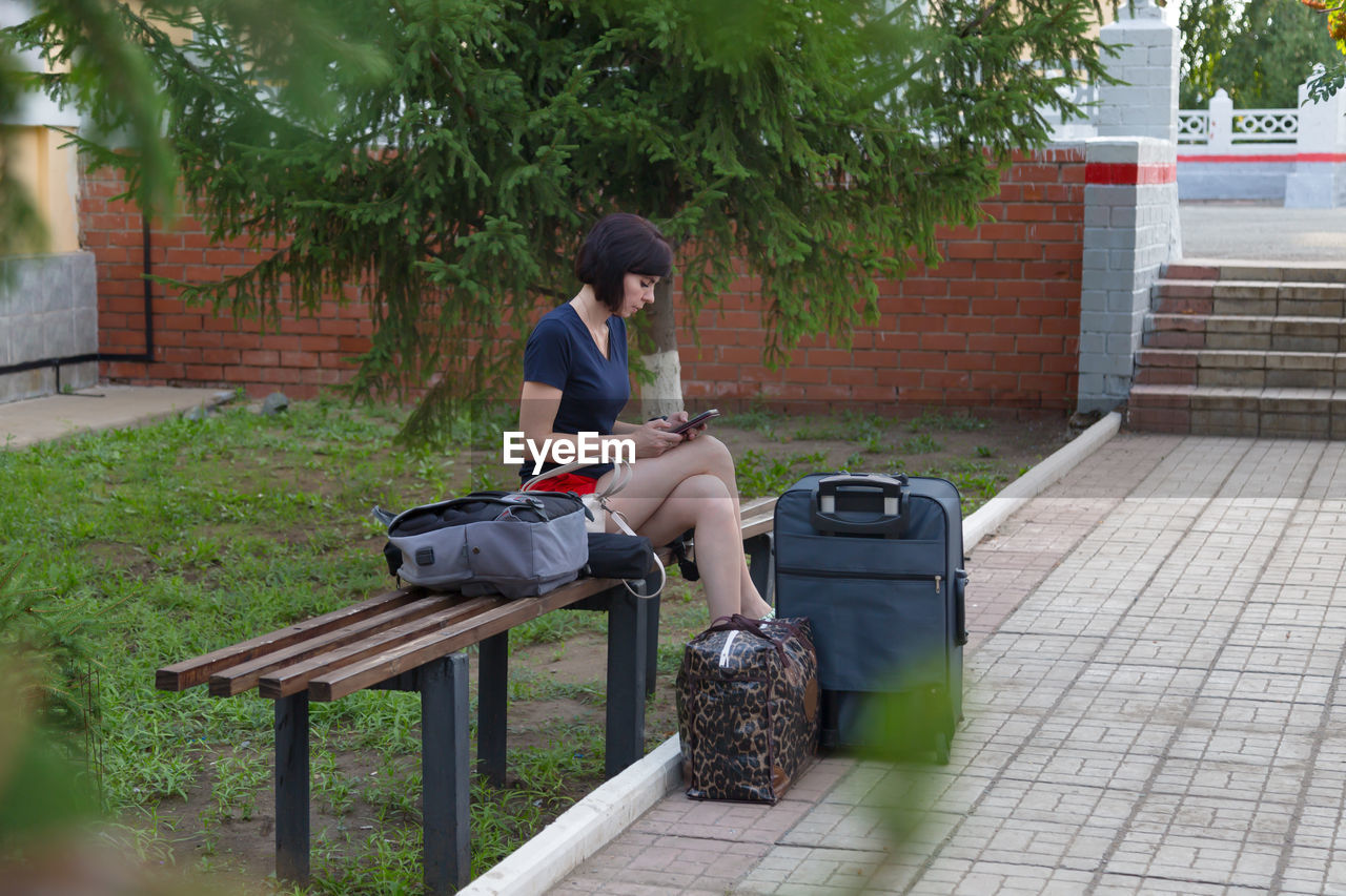 A happy brunette woman is sitting on a bench at the train station