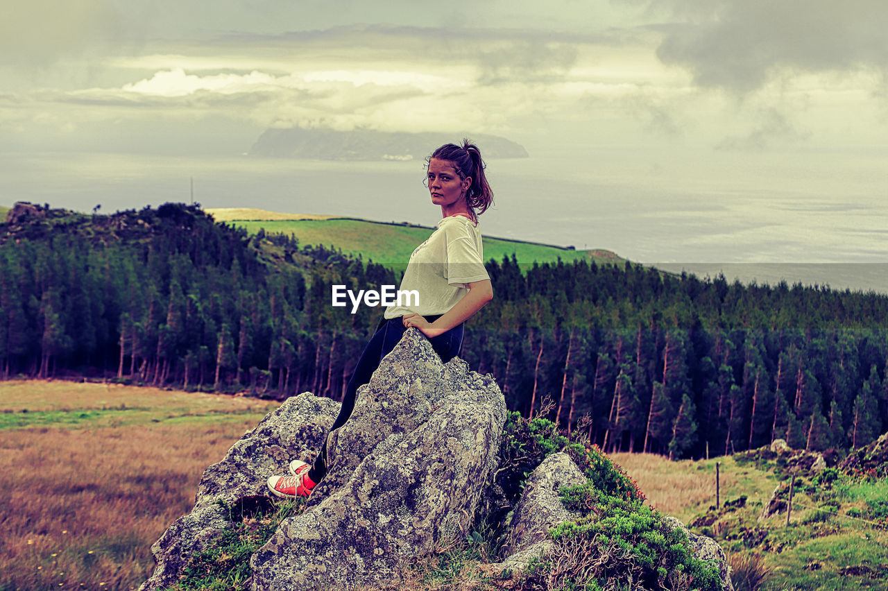 WOMAN STANDING ON ROCK AGAINST SKY