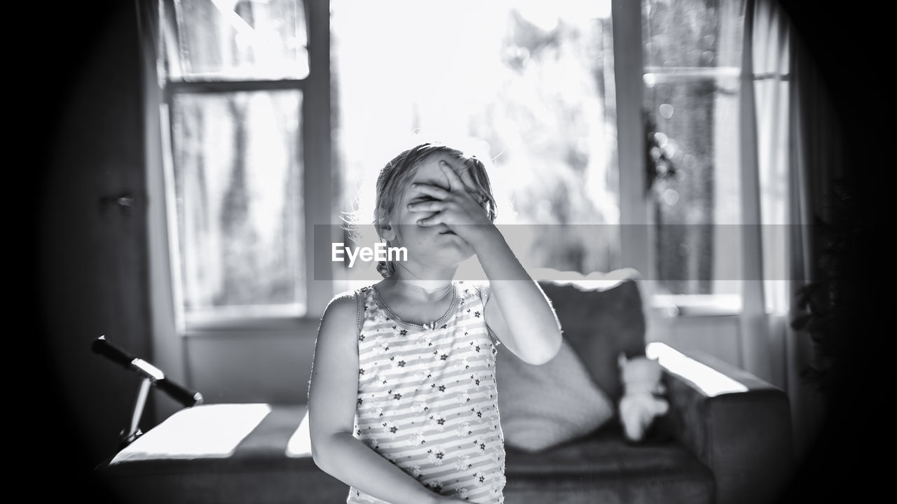 Girl covering face with hand while standing at home