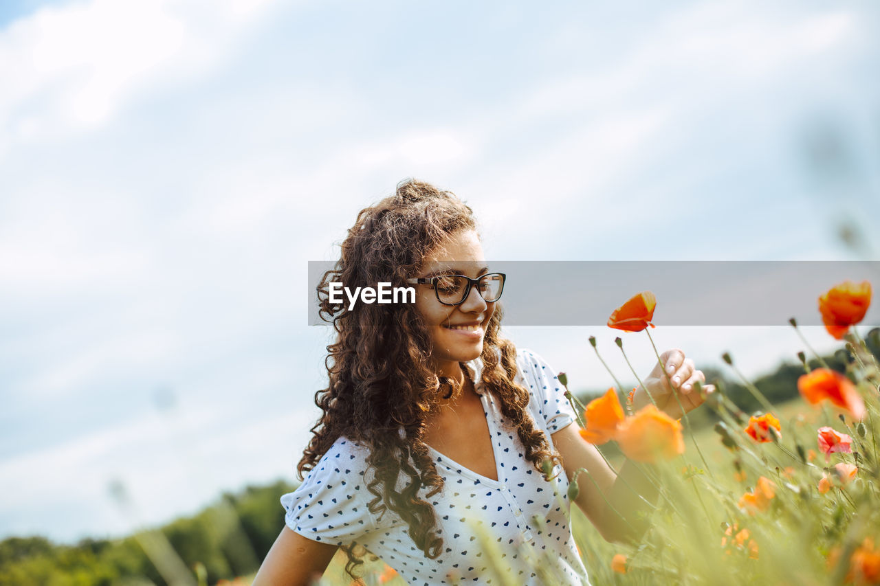 Smiling woman looking at flowers against sky