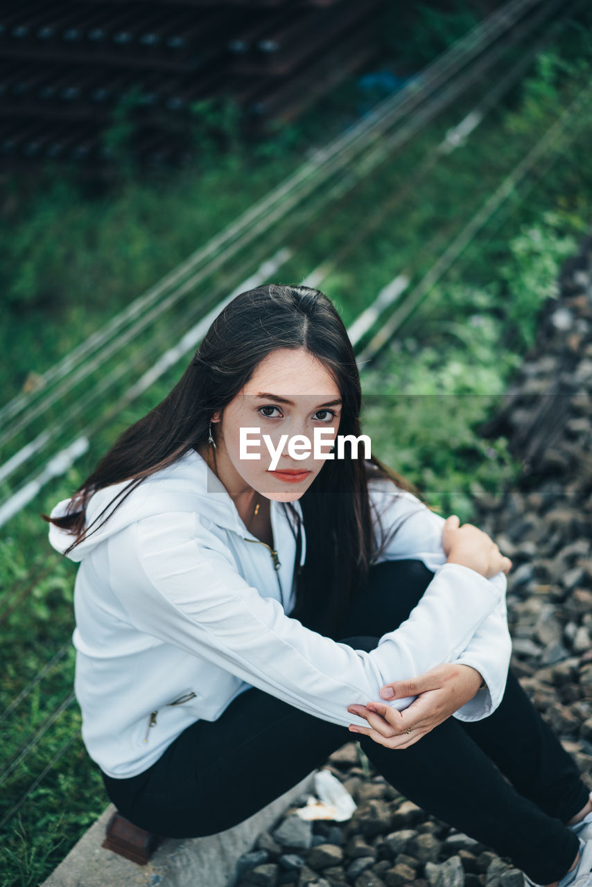 Portrait of young woman sitting on railroad track