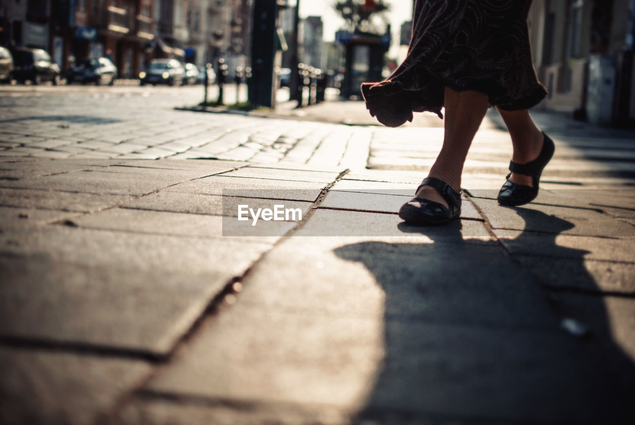 Low section of woman walking on sidewalk in city