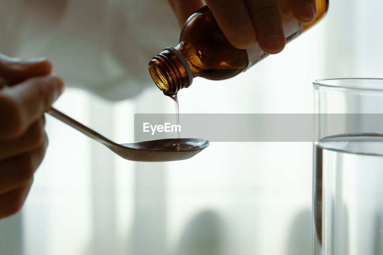 Woman hand pouring medication or cough syrup from bottle to spoo