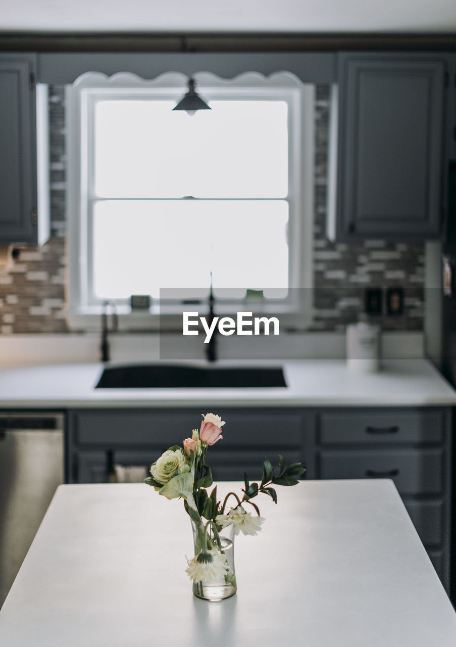 White kitchen countertop with flowers and vase and window in backgroun