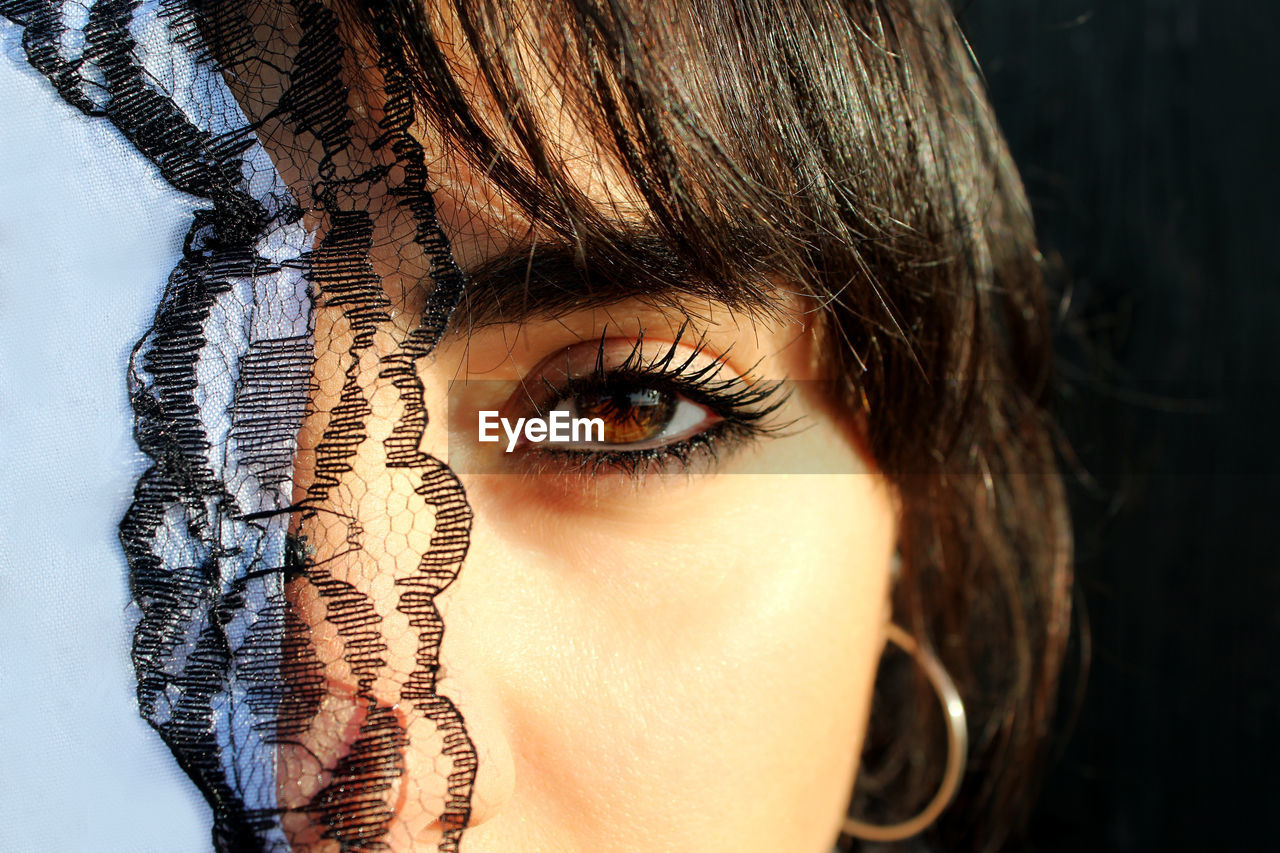 Close-up portrait of woman wearing mascara by textile in sunny day