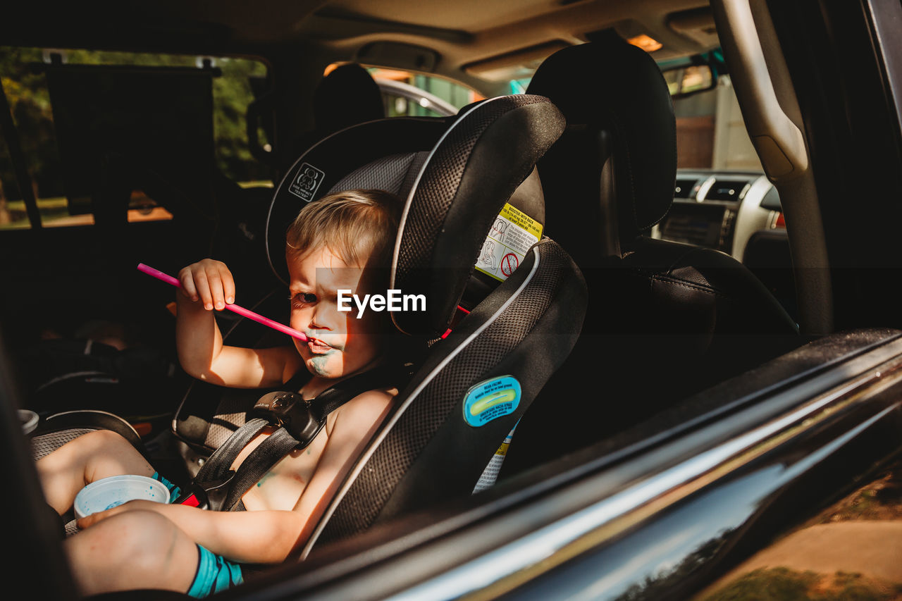 Young boy with grumpy face drinking from straw in car seat