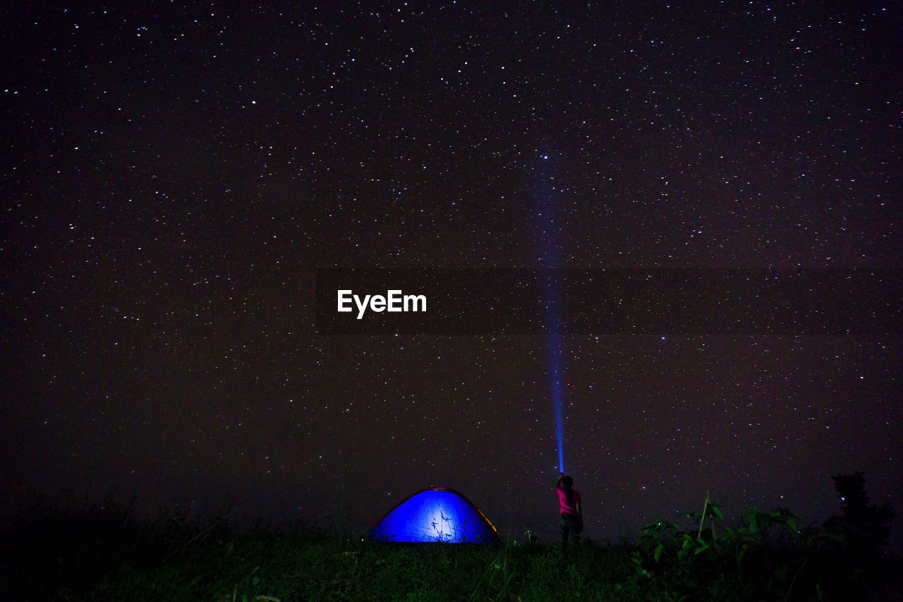 Woman with illuminated flashlight and tent against star field at night