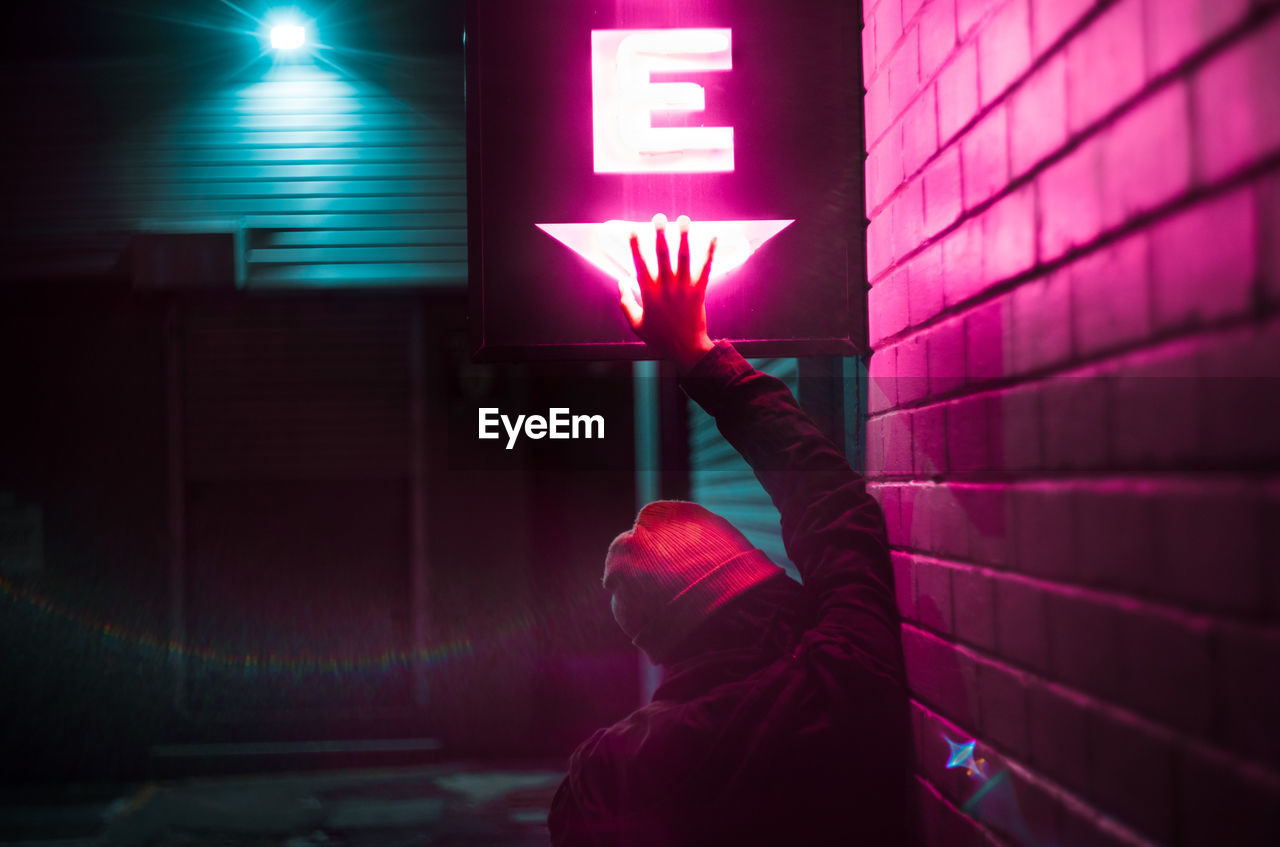 Rear view of woman touching neon sign by wall at night