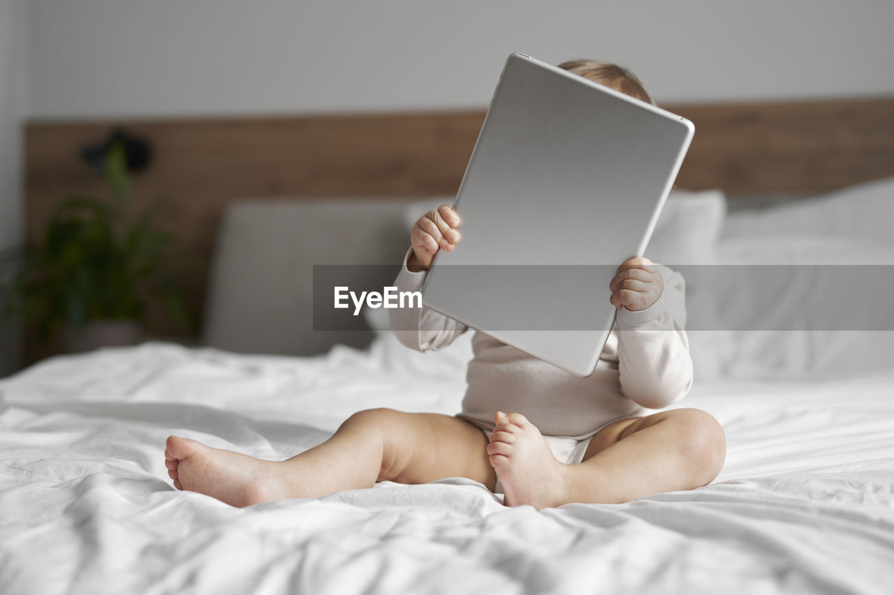 Cute girl holding digital tablet sitting on bed