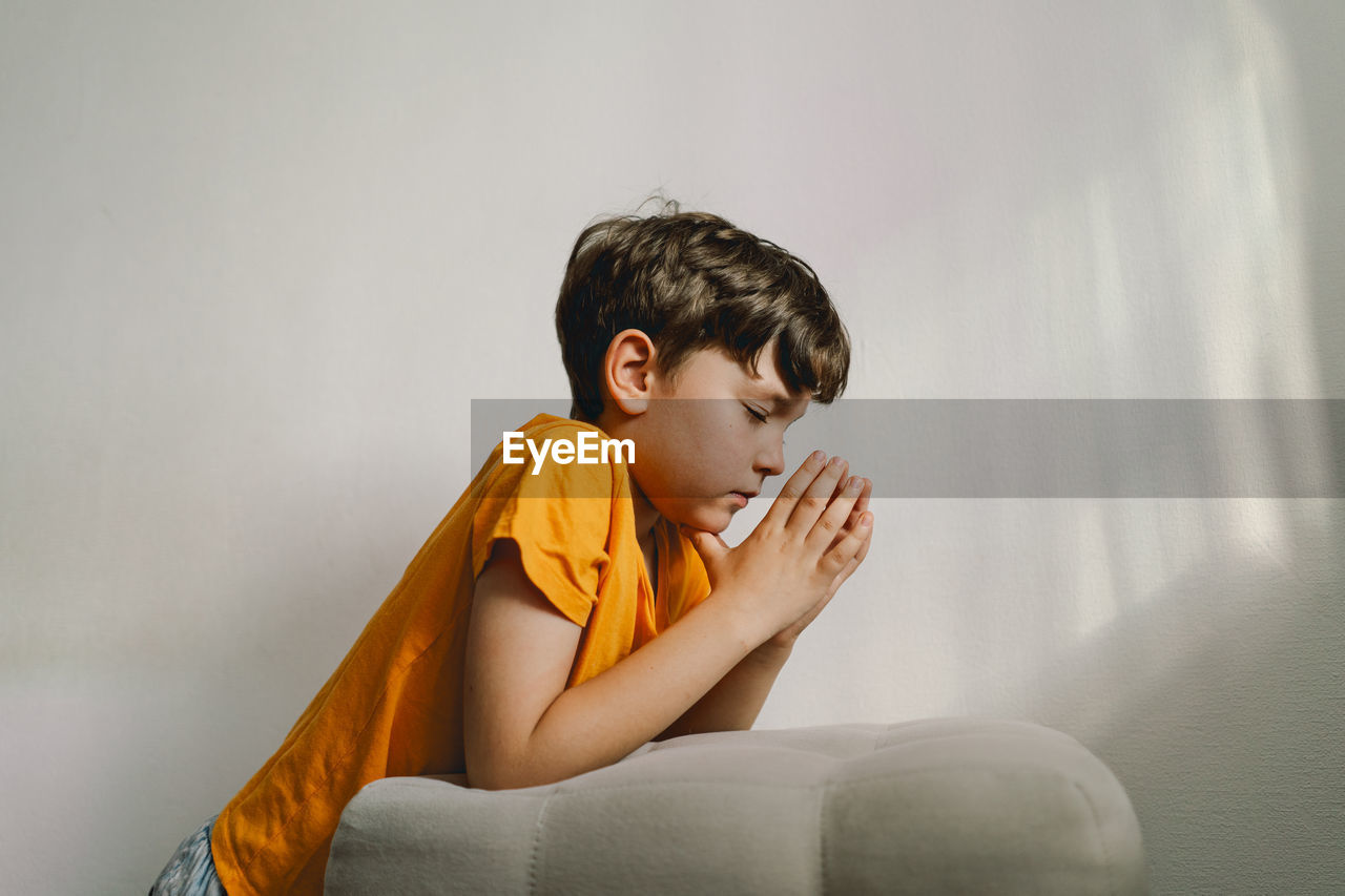 A boy in an orange t-shirt prays at home. concept for faith