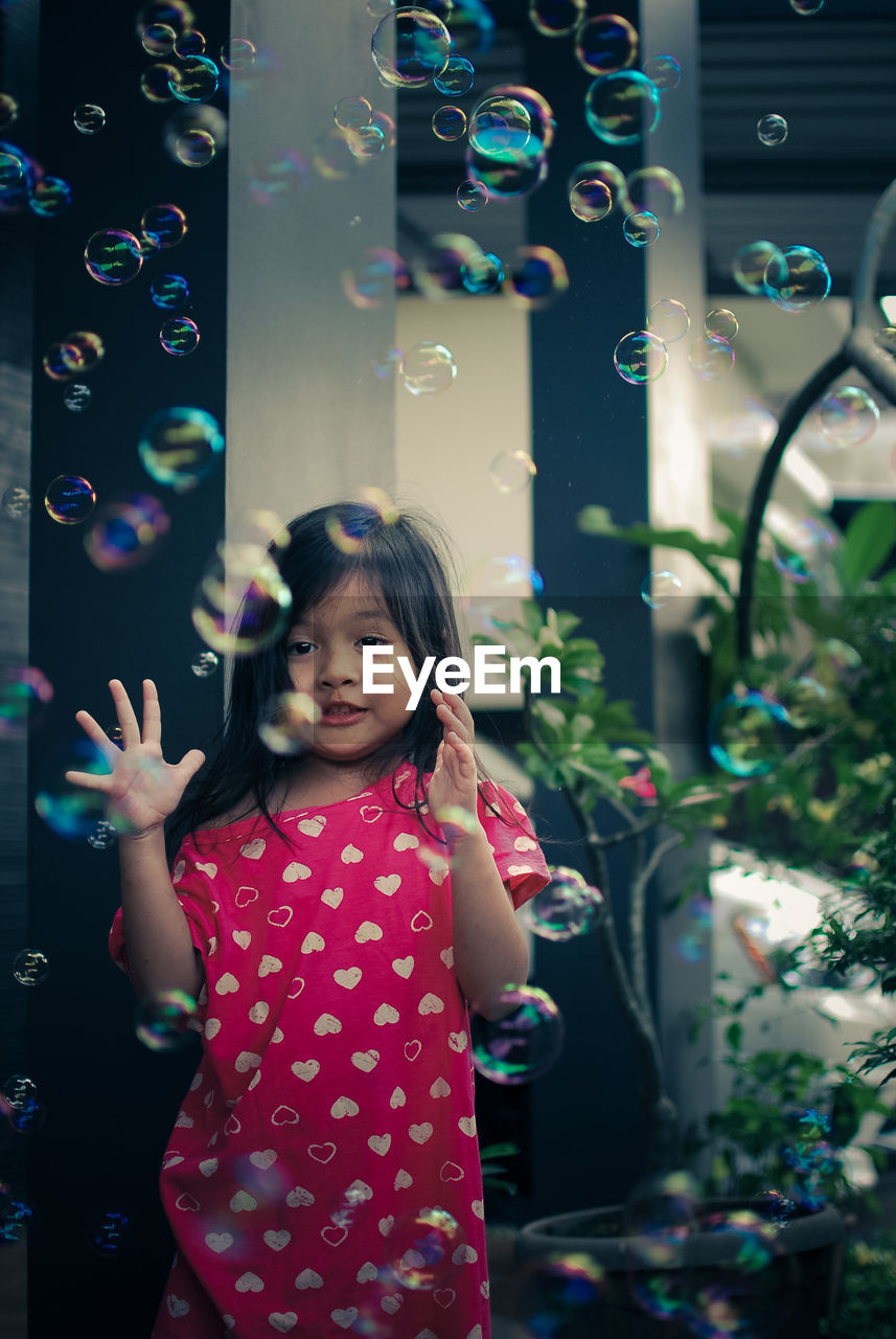Cute girl standing by bubbles flying in mid-air
