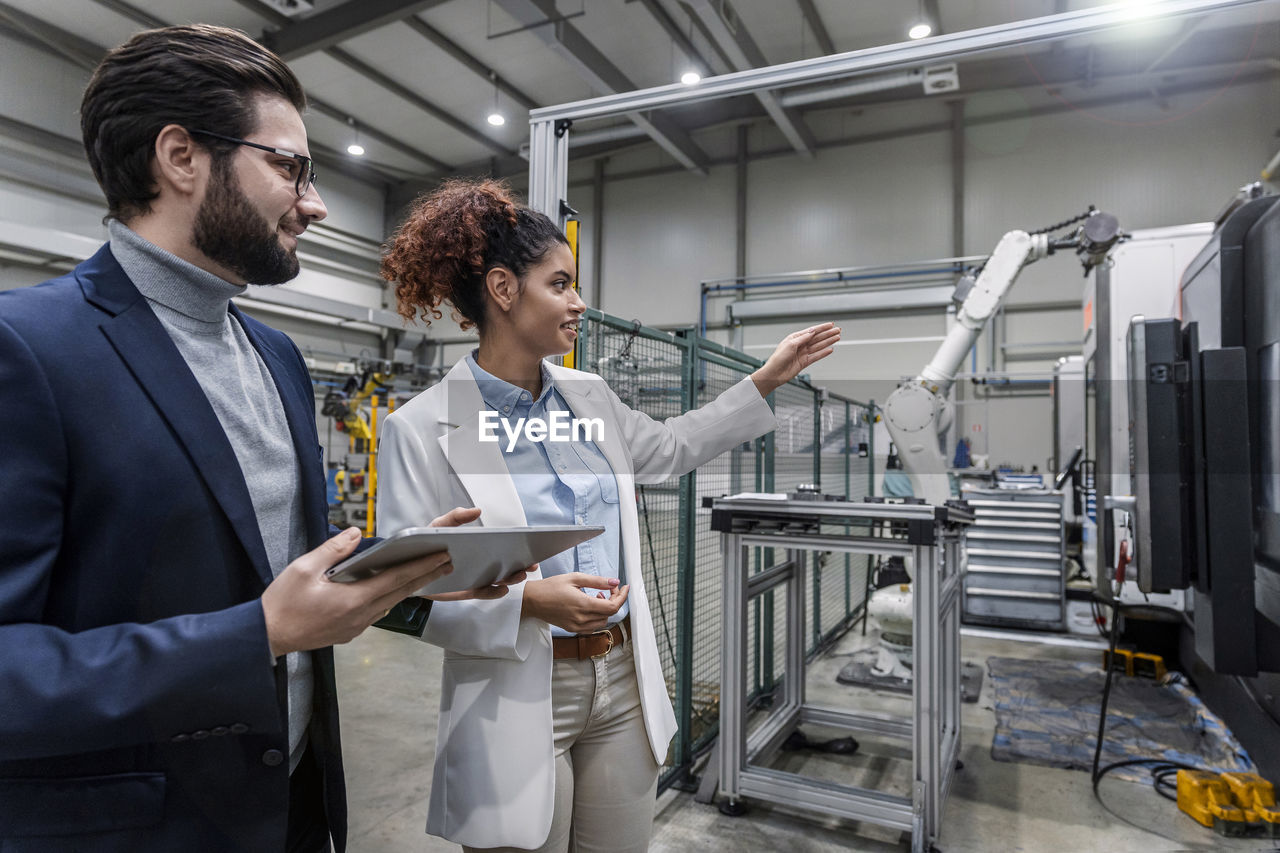 Engineers discussing over robotic arm in industry