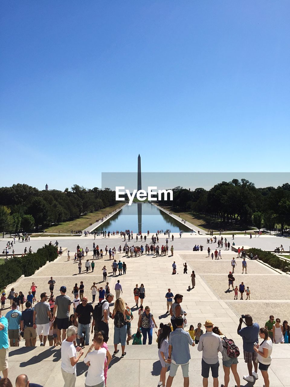 Crowd at lincoln memorial with washington monument reflection in pond against clear sky