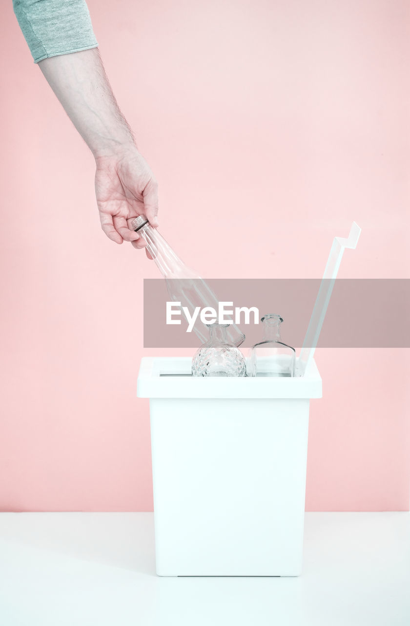 One person sorts recyclable materials on a pink background into a special bin for glass bottles