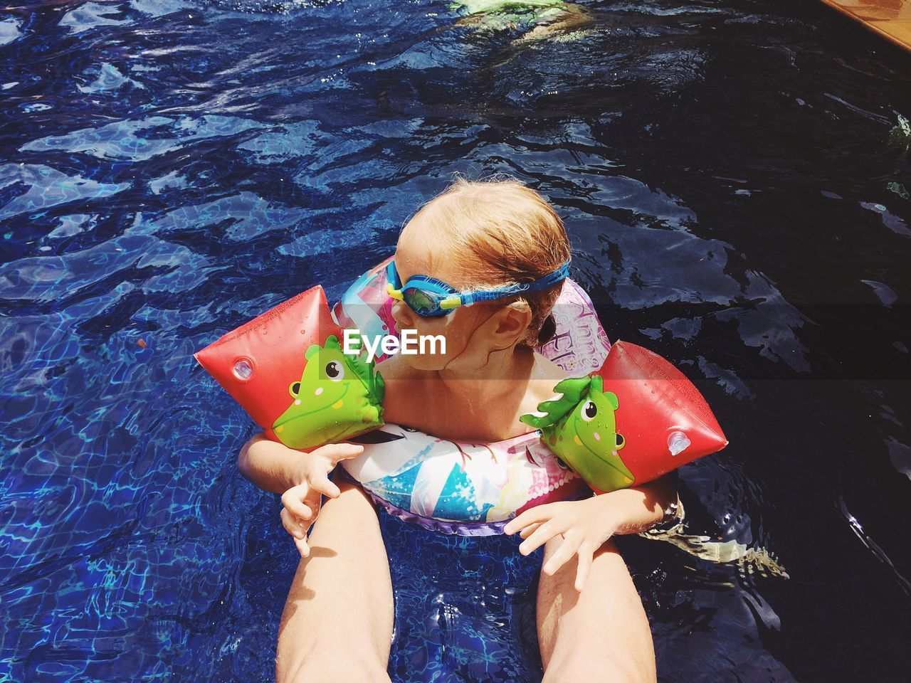 Low section of man by girl swimming in pool