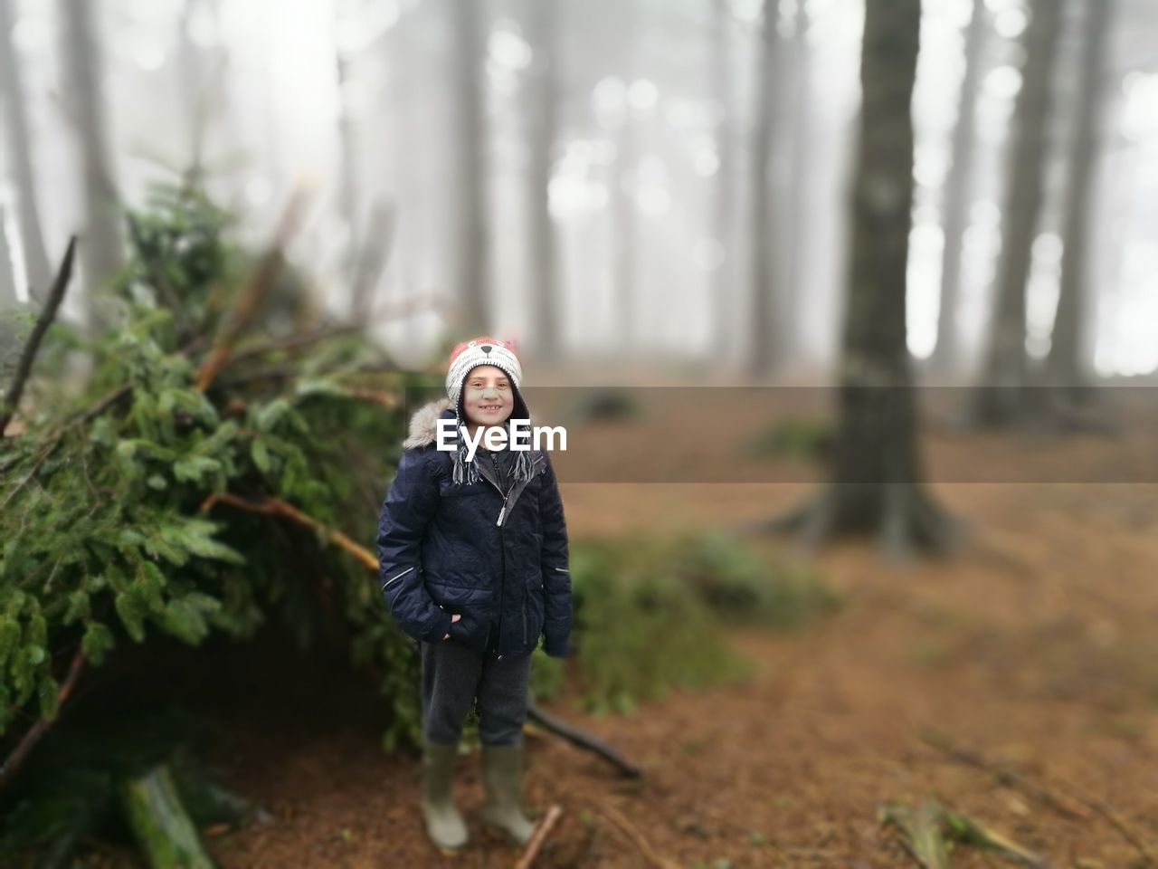 Tilt-shift portrait of smiling girl standing at forest during foggy weather