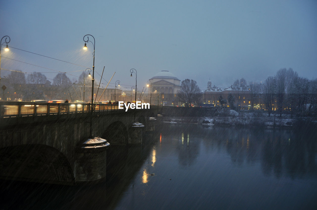 ILLUMINATED CITY BY RIVER AGAINST SKY