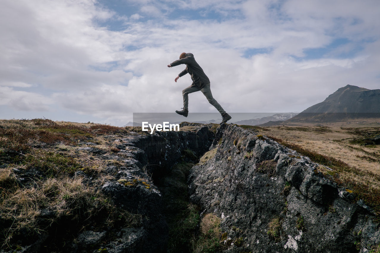 Side view of man on rock against sky