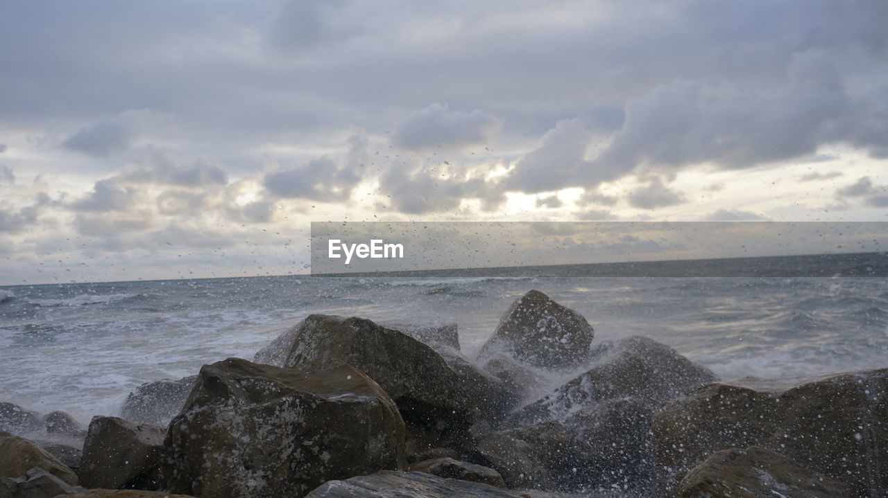 Scenic view of water splashing on rocks in sea against sky