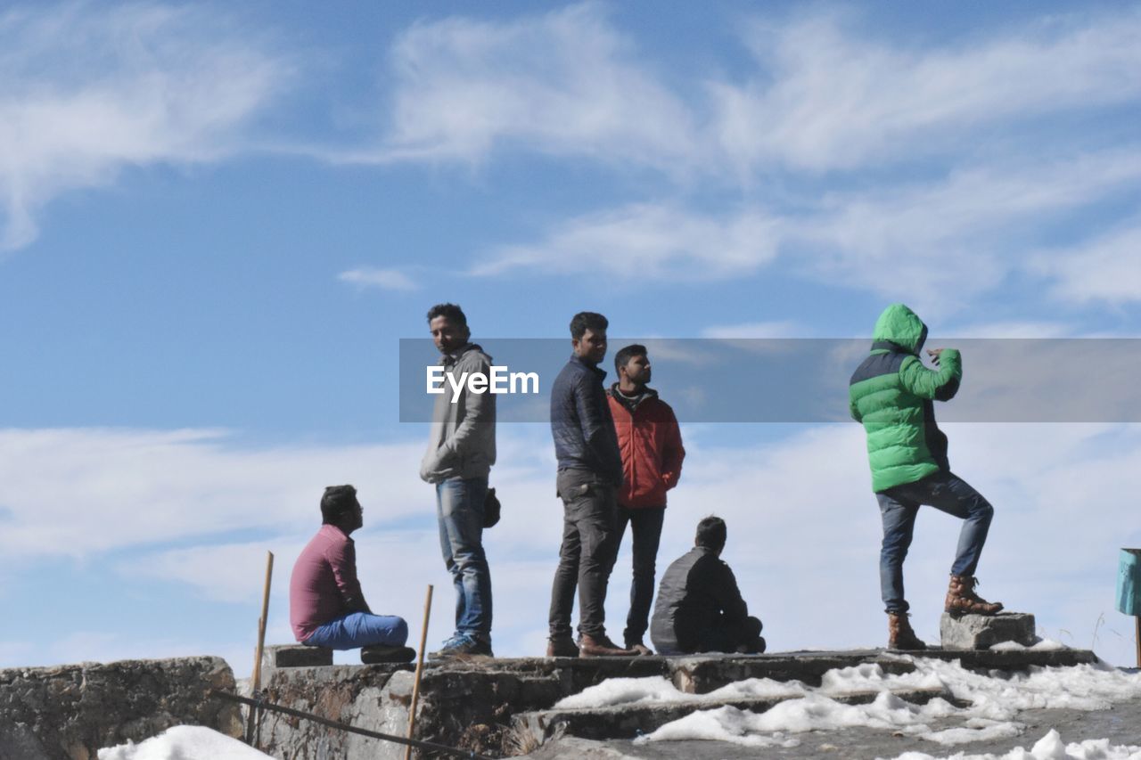 LOW ANGLE VIEW OF FRIENDS STANDING ON SNOW COVERED LANDSCAPE