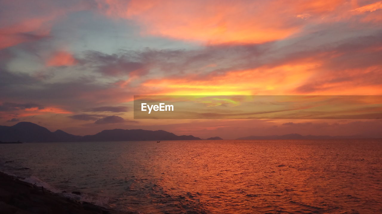 Scenic view of sea against dramatic sky during sunset