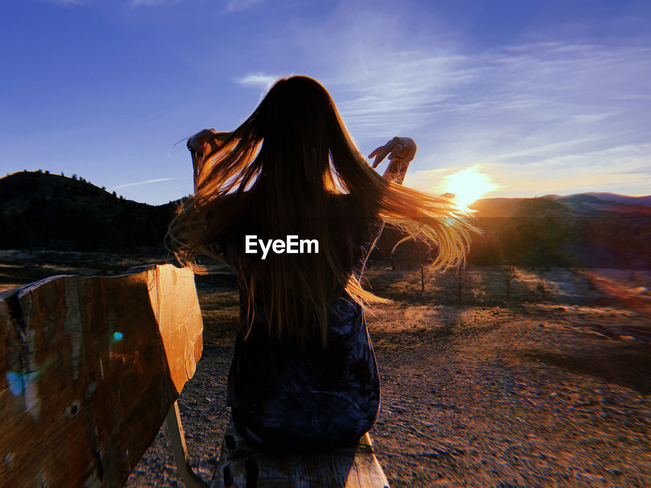 Rear view of woman sitting on bench against sky during sunset