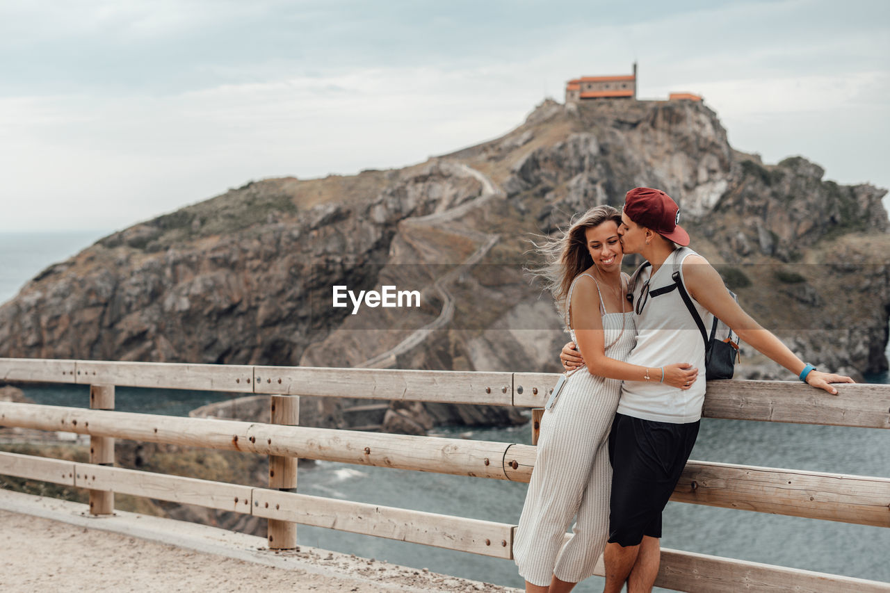 Couple embracing while standing by railing against sea